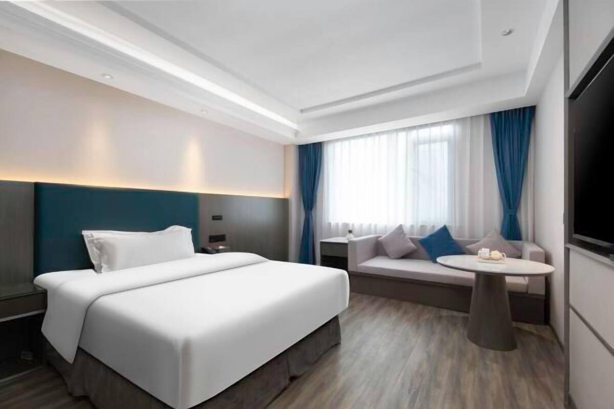 Una habitación de hotel moderna con una cama grande, un sofá, una mesita y un televisor.