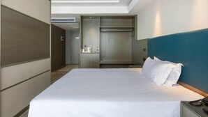 A modern hotel room with a large bed, a built-in wardrobe, and a kitchenette area.