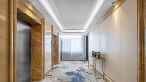 A hallway with a marble floor, a gold-framed elevator, and a small table with vases.