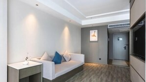 A modern hotel room with a white sofa, a side table, a flat-screen TV, and a wooden floor.