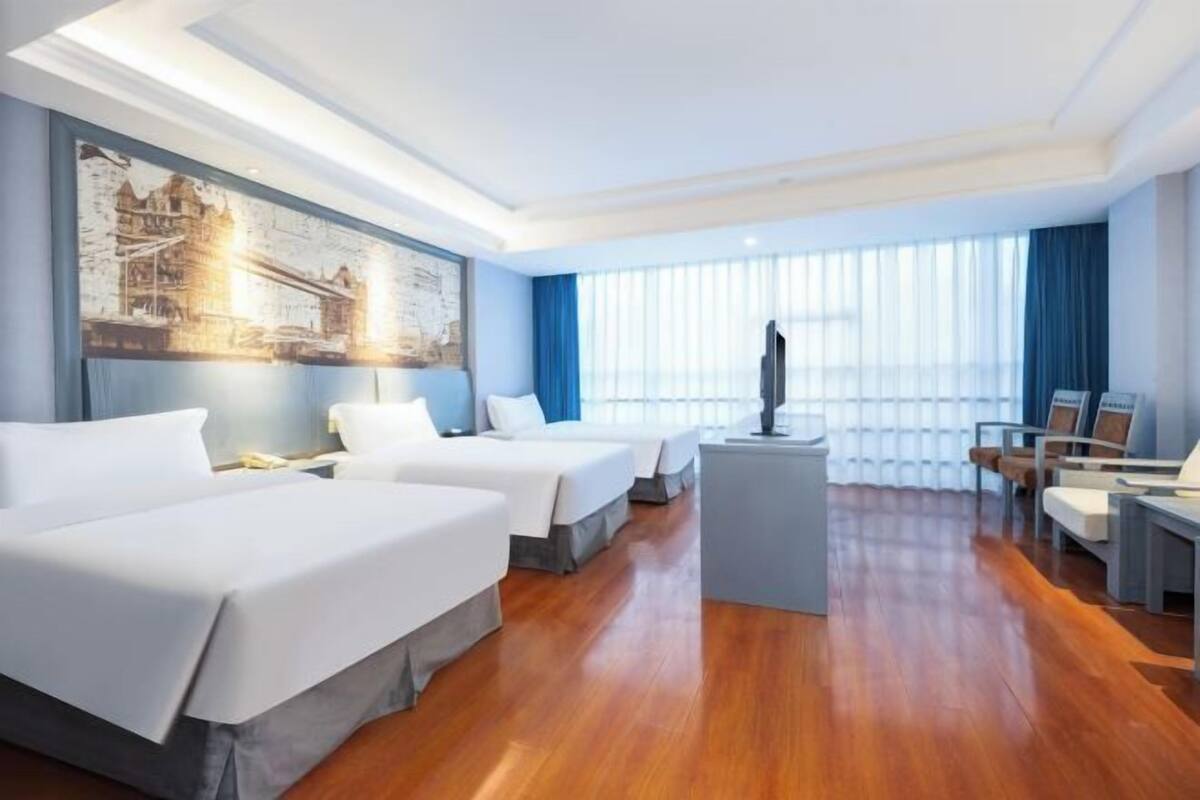 Una habitación de hotel con dos camas, un escritorio, un televisor y un amplio ventanal con cortinas.