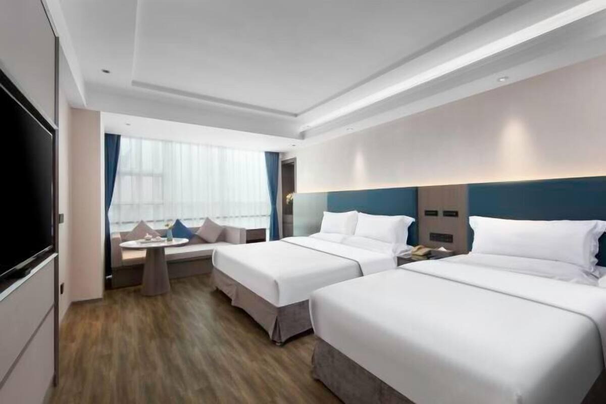 Una habitación de hotel con dos camas, televisor, una mesita y ventana con cortinas.