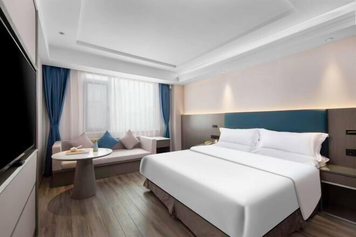 Habitación de hotel con una cama grande, un sofá, una mesita redonda y un televisor.
