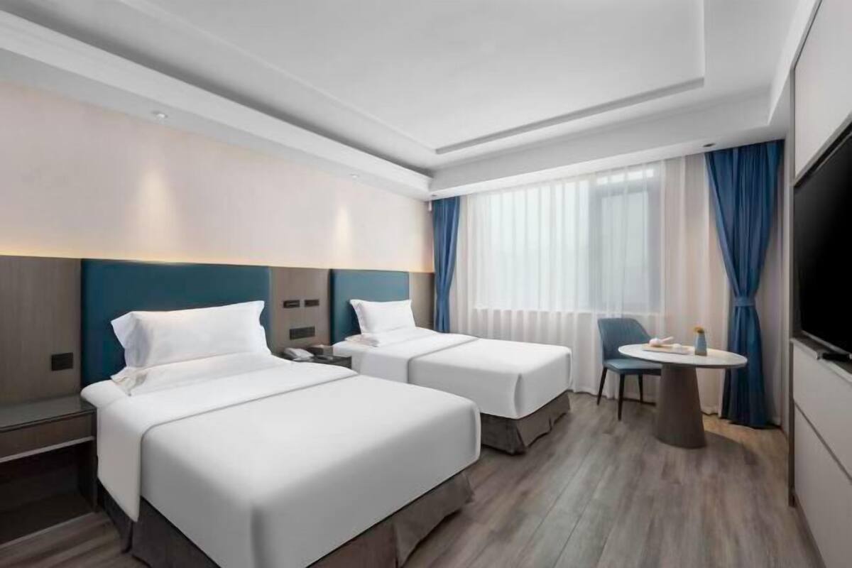 Una habitación de hotel con dos camas, una mesita, una silla y un televisor.