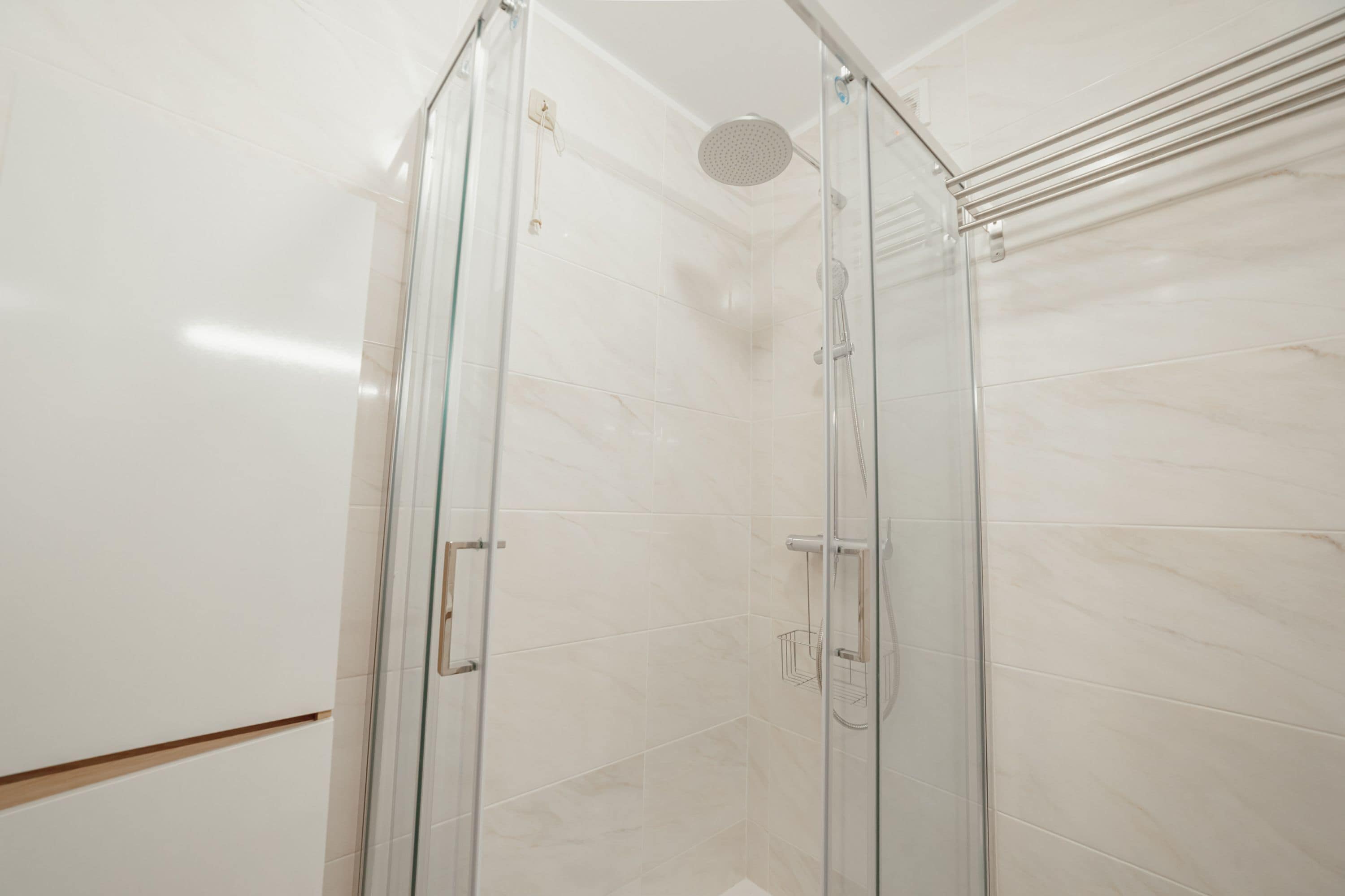 A glass-enclosed shower with a handheld showerhead and a wall-mounted faucet.