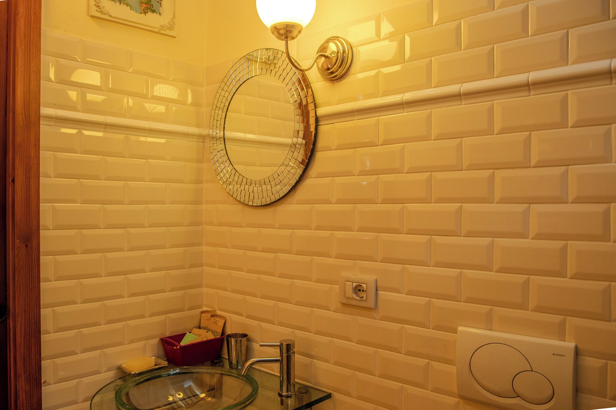 Un bagno con parete rivestita di piastrelle bianche, uno specchio rotondo, un lavabo in vetro e un lampadario.