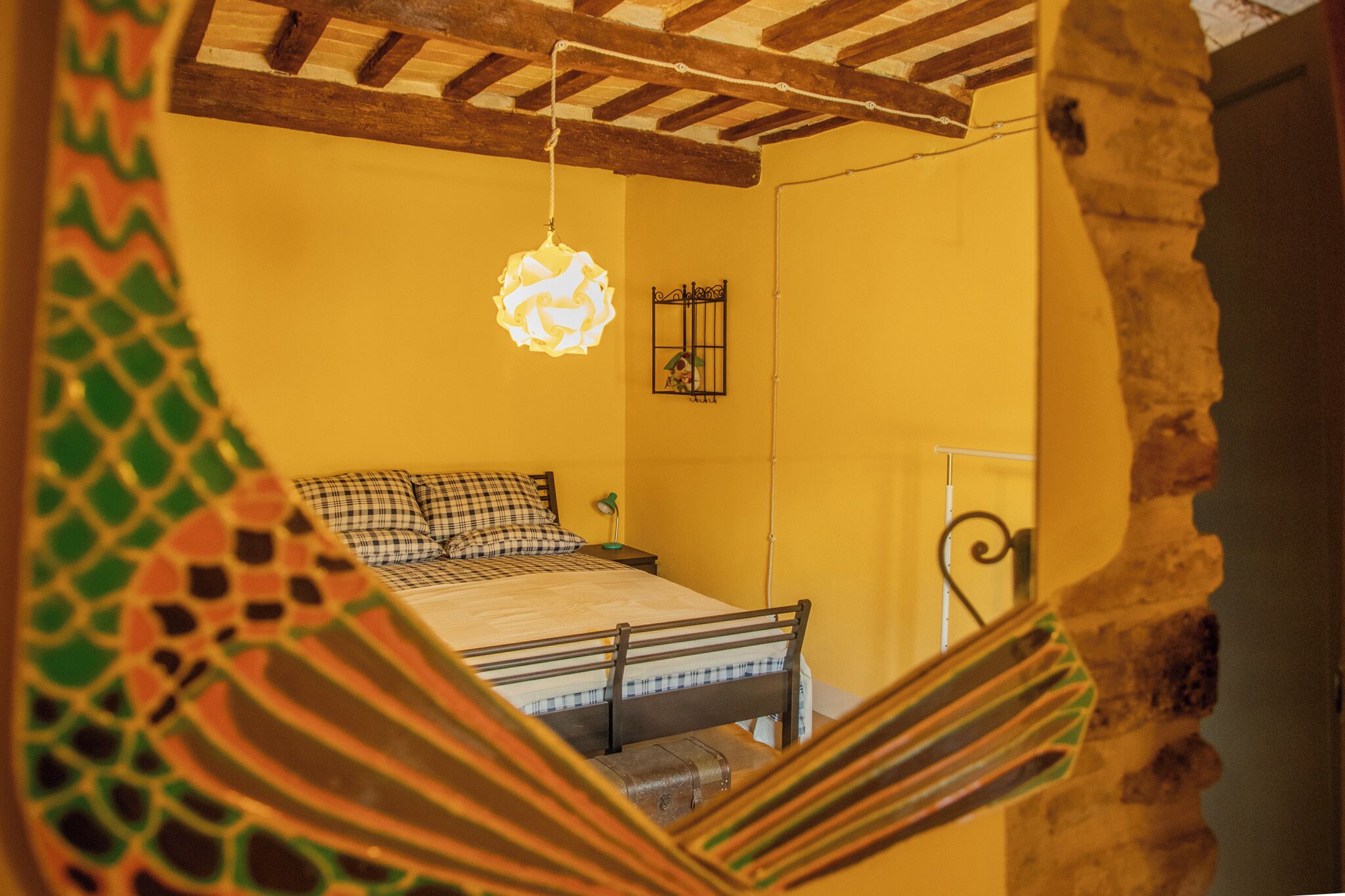 Una habitación con una cama, un candelabro colgante, una mesita con lámpara y un adorno en la pared.
