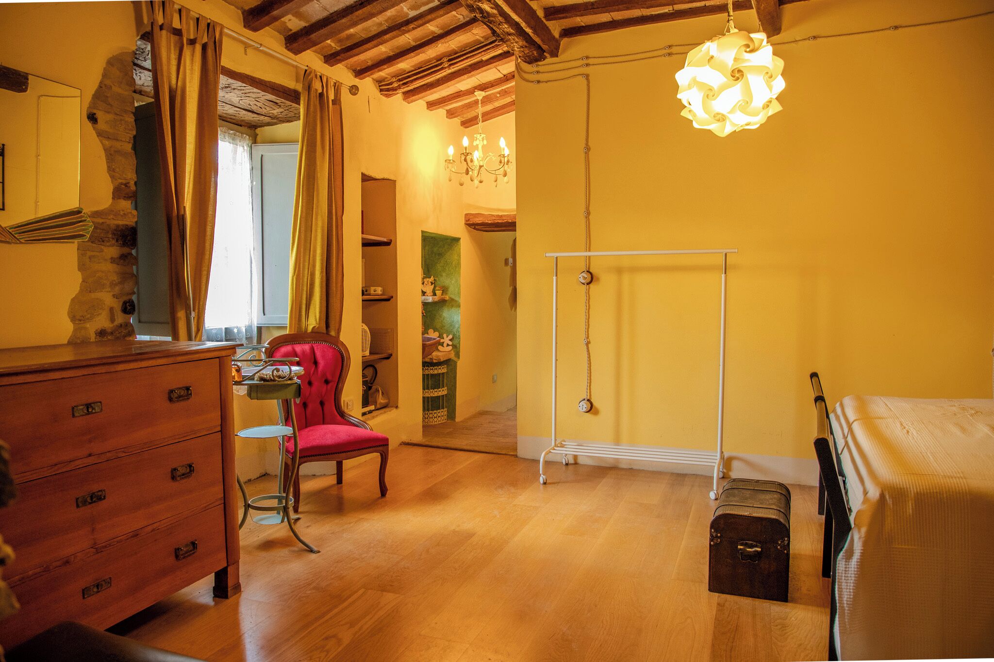 A room with a wooden dresser, a red chair, a bed, a suitcase, and a wardrobe.