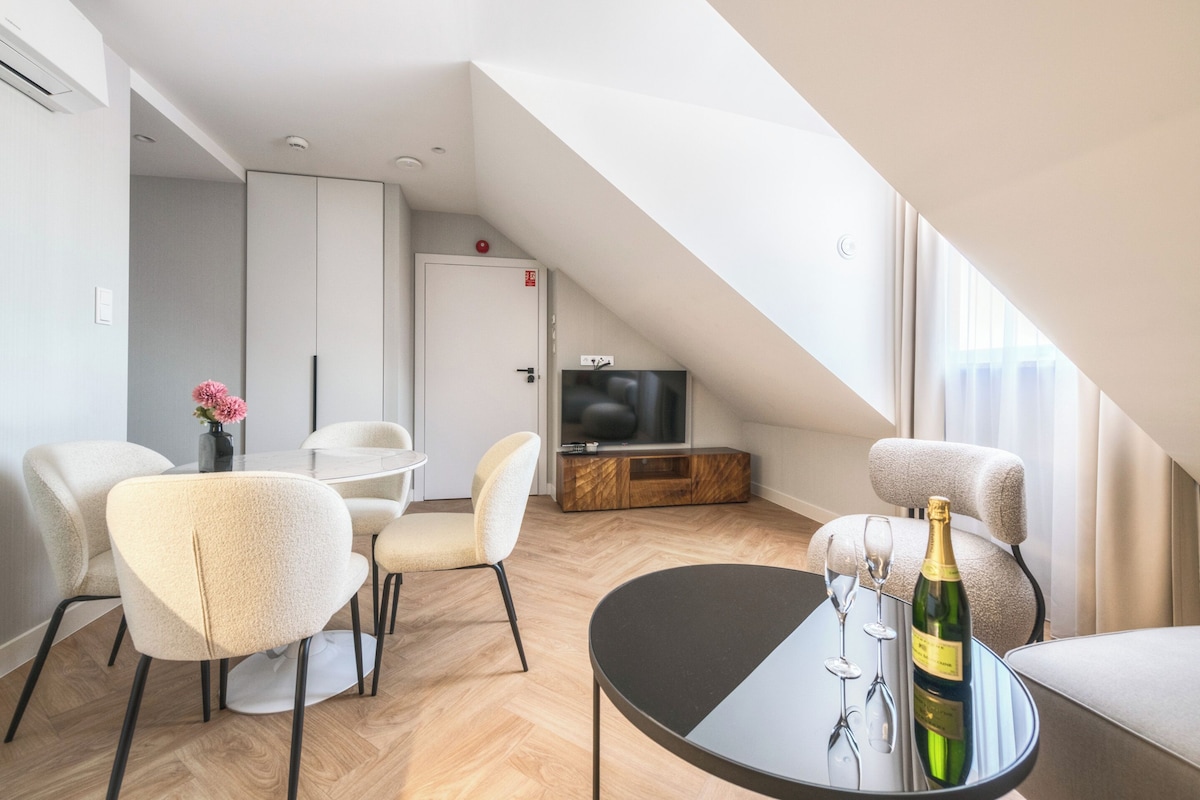 Una sala de estar moderna con comedor, televisor y una botella de champán sobre una mesa.