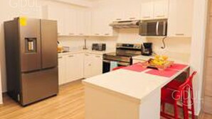 A modern kitchen with white cabinetry, stainless steel appliances, and a central island with a red chair. - Cozy, Modern APT @ Col. Escalon - Pool, Gym, A/C (San Salvador)