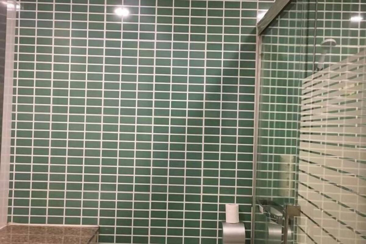 A bathroom with green tiled walls and a glass shower enclosure.
