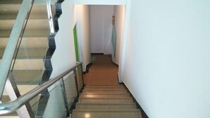 Uma escadaria com guarda-corpos de vidro e degraus revestidos de carpete bege, levando a um corredor.