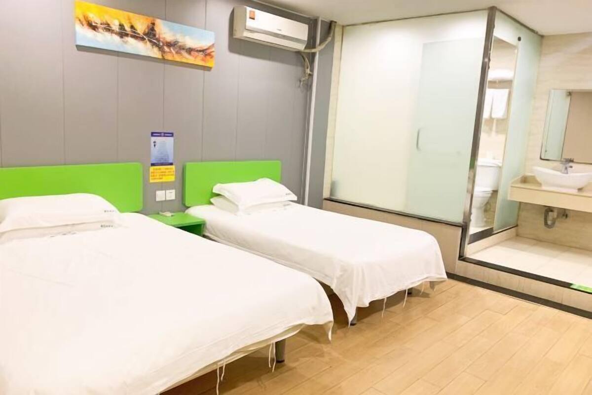A hotel room with two beds, a bathroom with a sink and mirror, and a shower.