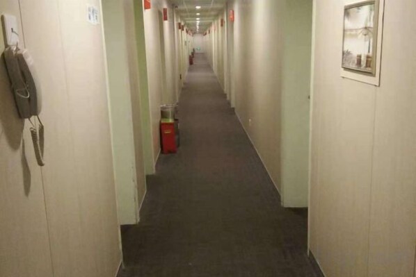 En lang, smal hotelsgang med døre på begge sider, en skraldespand i midten og en telefon på venstre væg.