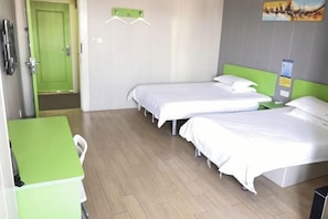 A hotel room with two beds, a desk, and a green door.