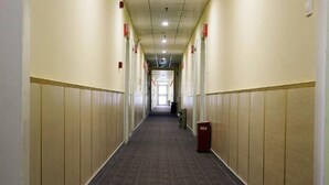 Um corredor de hotel comprido e estreito, com piso coberto de carpete e painéis de madeira nas paredes.