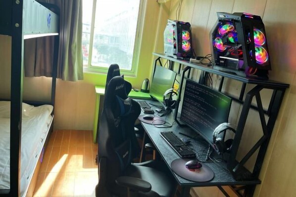 Una habitación con literas, un escritorio con computadora, y una ventana con vista a edificios.