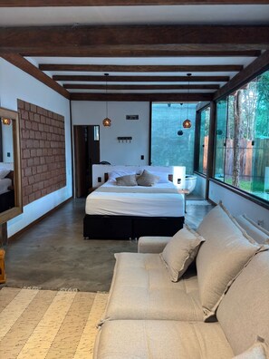 A modern bedroom with a large bed, a sofa, and a view through large windows.