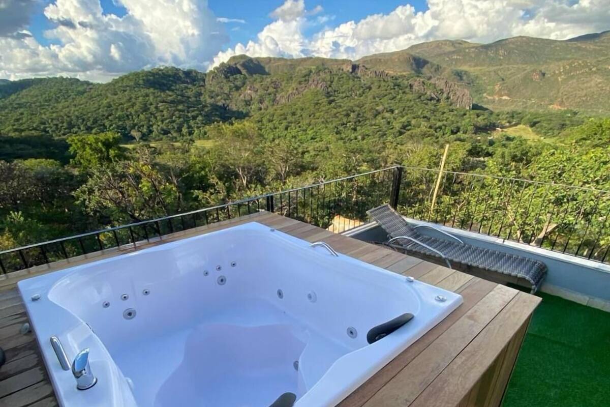 A hot tub on a wooden deck with a view of green hills and a clear sky.