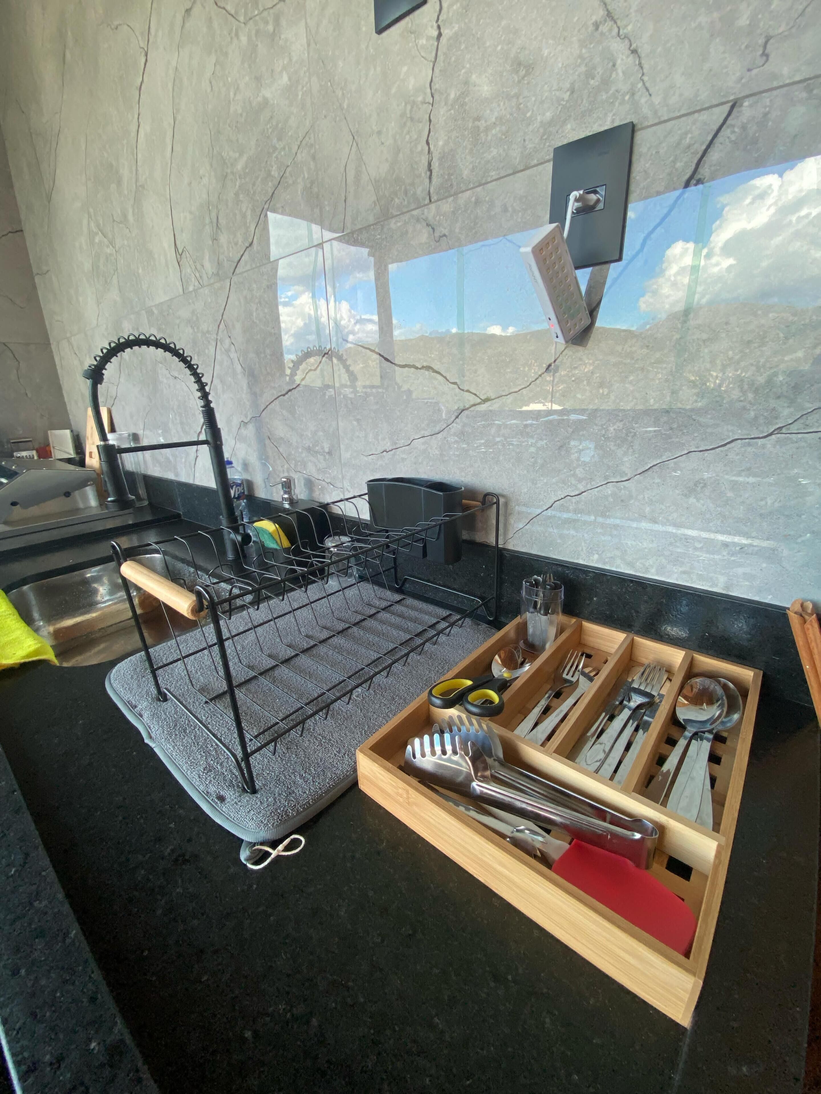 A kitchen with a marble backsplash, a black countertop, and a wooden utensil organizer.