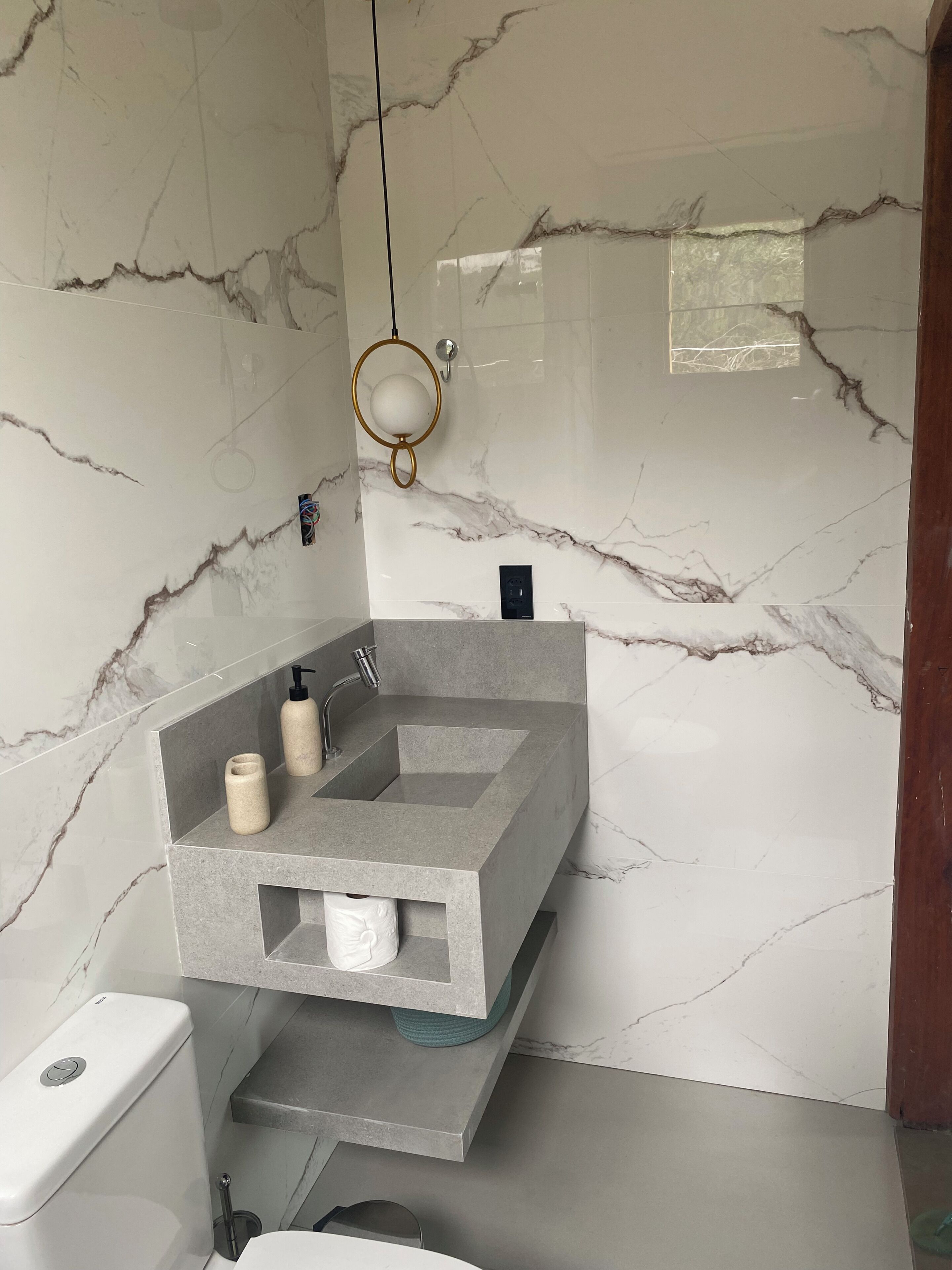 Et badeværelse med marmorvæg, en indbygget grå vask, toilet og et håndklædestativ.