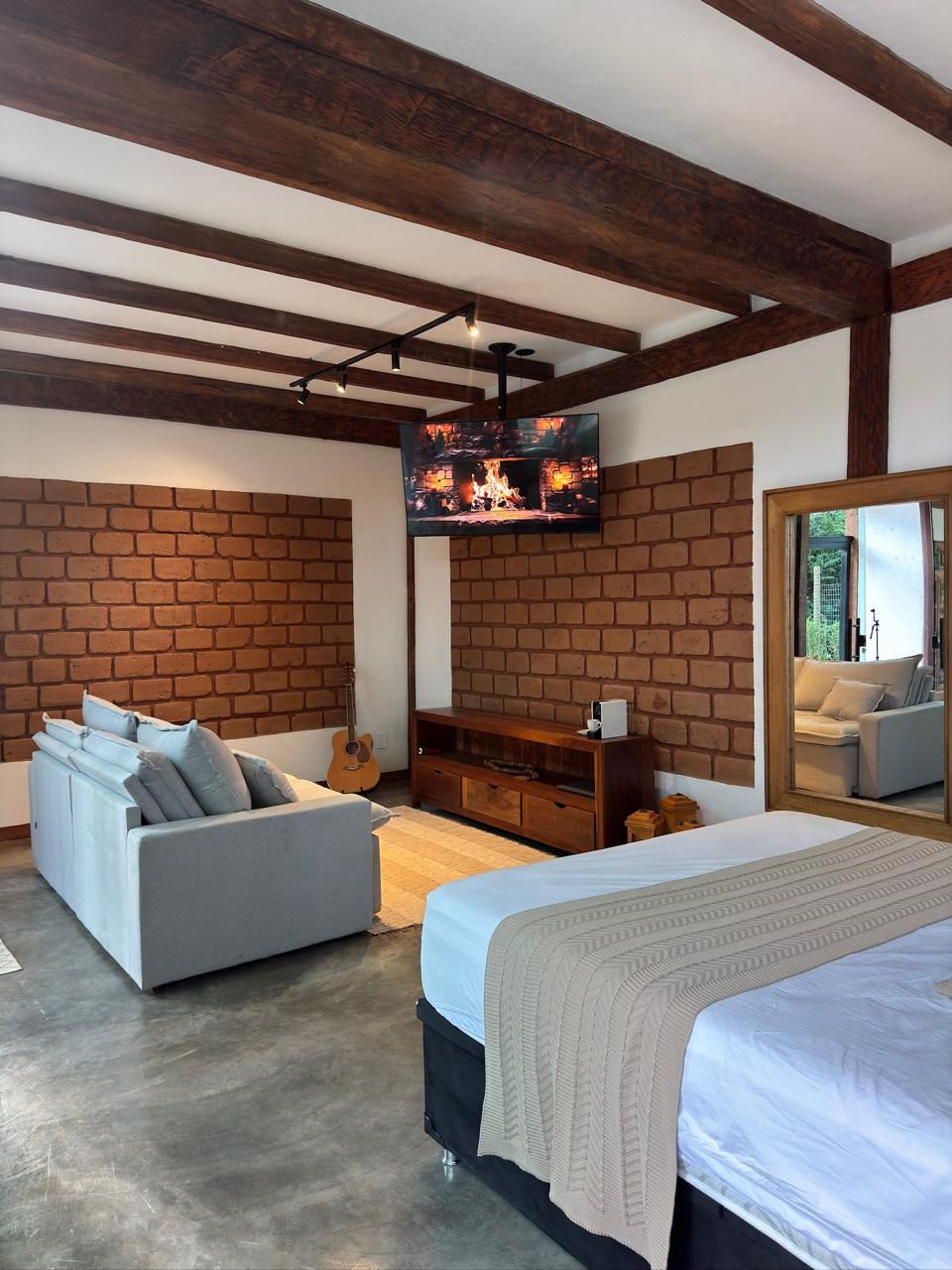 A bedroom with a brick wall, a sofa, a bed, a TV, and a mirror.