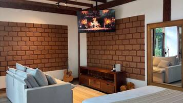 A bedroom with a brick wall, a sofa, a bed, a TV, and a mirror.