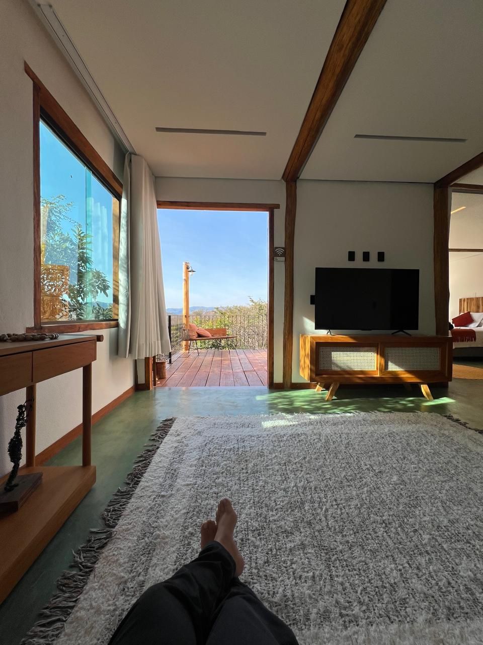 A spacious room with a large window, a flat-screen TV, and a wooden floor.
