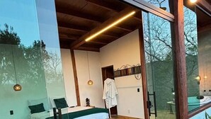 A modern room with a bed, a bench, a table, and a glass door leading to an outdoor area. - Reserva Cipó (Santana do Riacho)