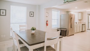 Een moderne keuken met witte kastjes, een roestvrijstalen koelkast en een eetgedeelte met een houten tafel en witte stoelen.
