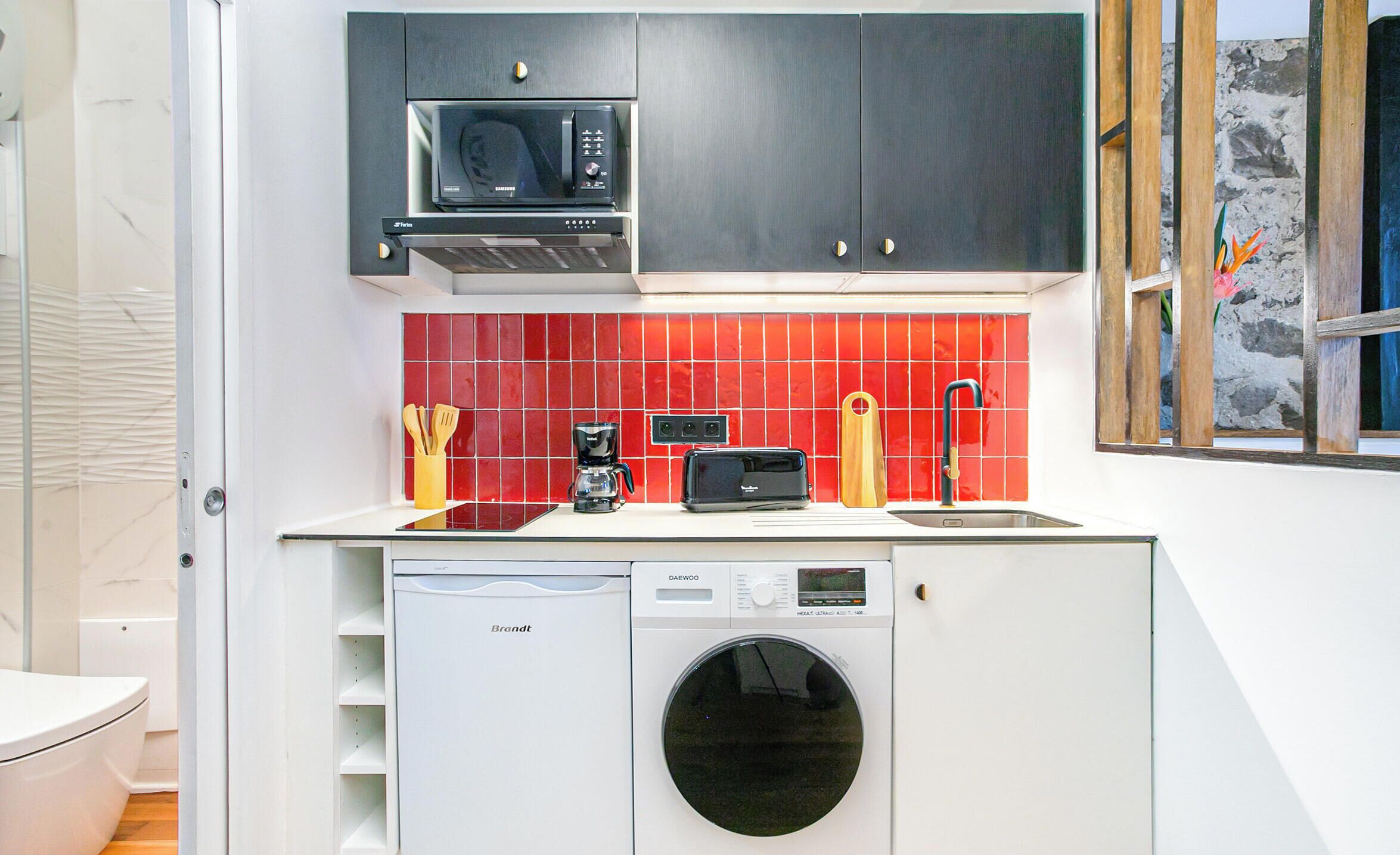 A compact kitchen with a microwave, coffee maker, and washing machine.