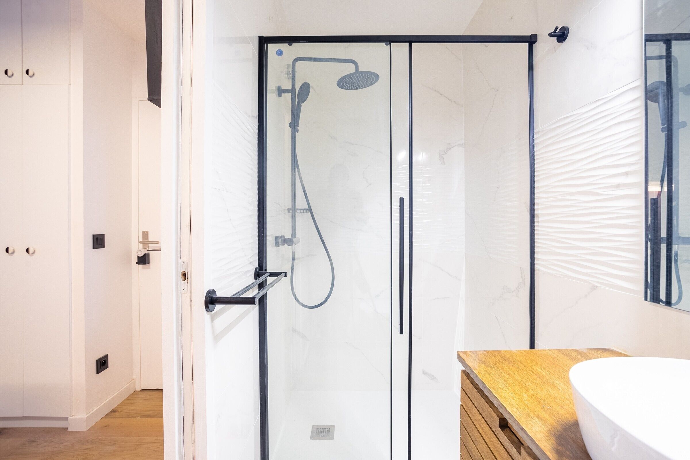 Un bagno moderno con cabina doccia in vetro, mobile lavabo in legno e pannello di marmo.
