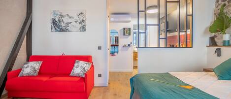 A modern bedroom with a red sofa, a bed with a green bedspread, and a large mirror.