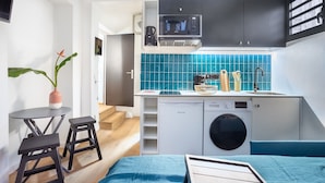 A compact kitchen with a microwave, sink, and washing machine. There is a small dining area with stools and a table. - Residence Nokoshima (Fort-de-France)