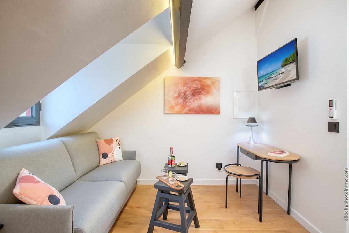 Una sala de estar moderna con un sofá, una mesita con una lámpara, un cuadro y un televisor en la pared.