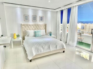A modern bedroom with a large bed, a bedside table, a small desk, and a view of the outside. - Blue Bliss Studio ISLA VERDE with parking & pool (Carolina)
