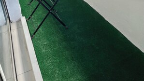 A balcony with artificial green turf, a wooden table, and chairs.