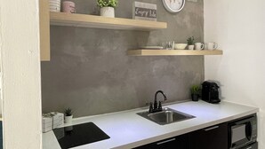 A kitchen with a stainless steel sink, a microwave, and a coffee maker. There are two wooden shelves above the counter, each holding various kitchen items.