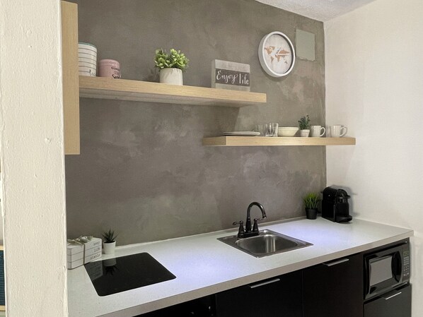 A kitchen with a stainless steel sink, a microwave, and a coffee maker. There are two wooden shelves above the counter, each holding various kitchen items. - Blue Bliss Studio ISLA VERDE with parking & pool (Carolina)