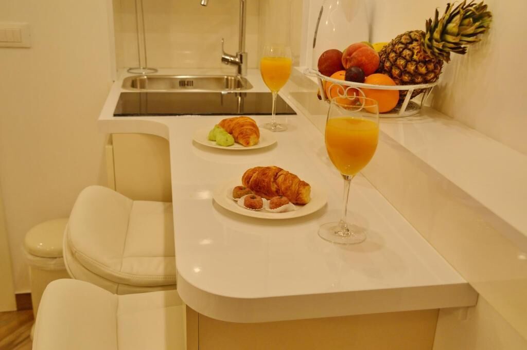 Une cuisine moderne avec un plan de travail blanc, un évier et un panier de fruits contenant des oranges et un ananas.