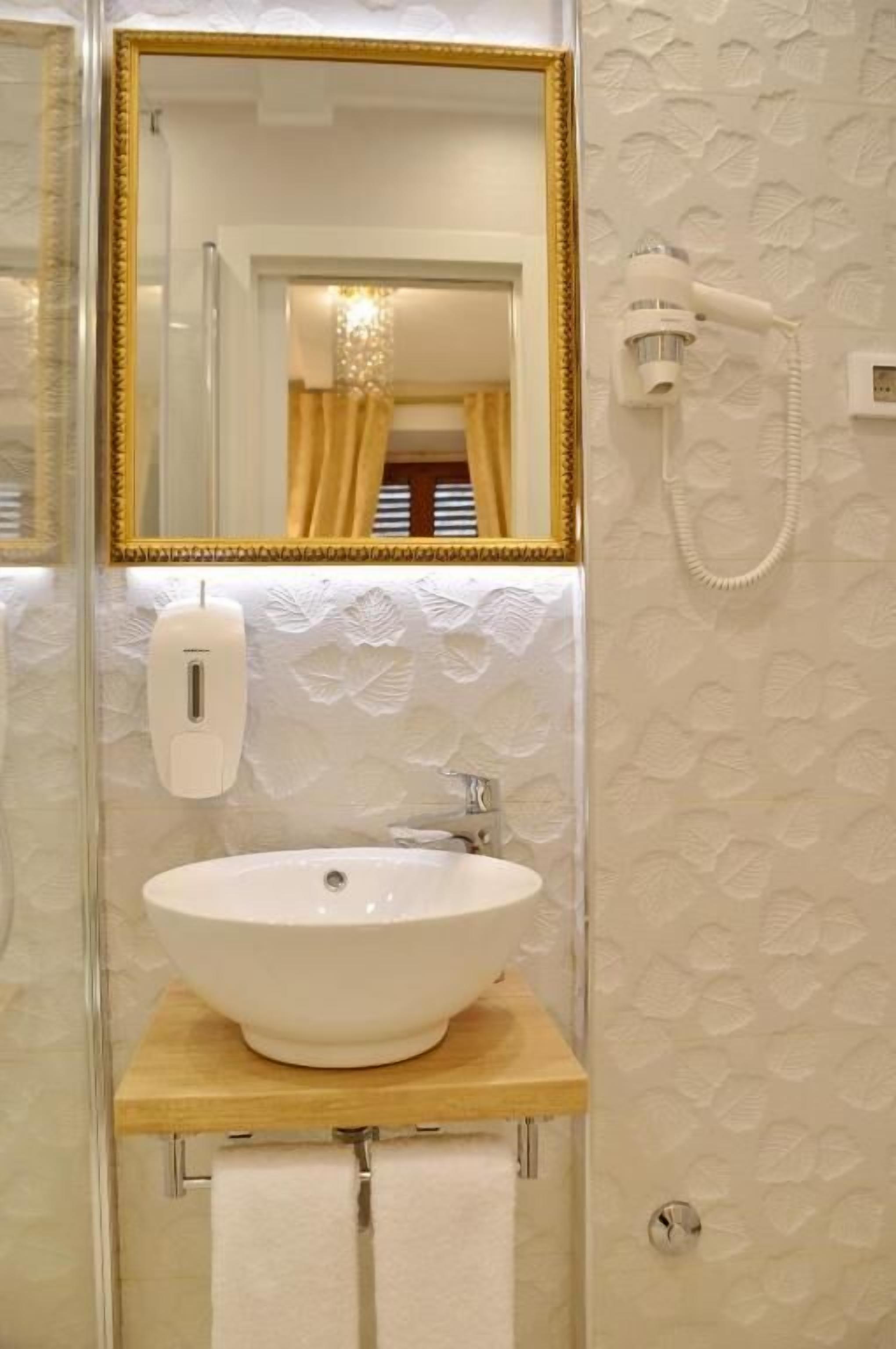 A bathroom with a white sink, a gold-framed mirror, a handheld hair dryer, and a towel rack.