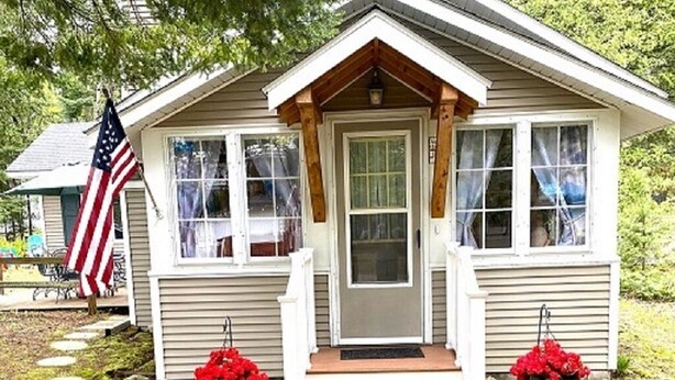 Een klein, gelijkvloers huis met een veranda, een voordeur en een kleine tuin met staptegels en potplanten.