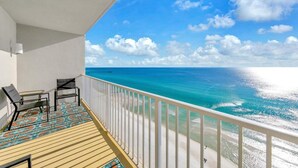 Un balcon avec deux chaises et une table, donnant sur une mer d’un bleu limpide et une plage de sable.