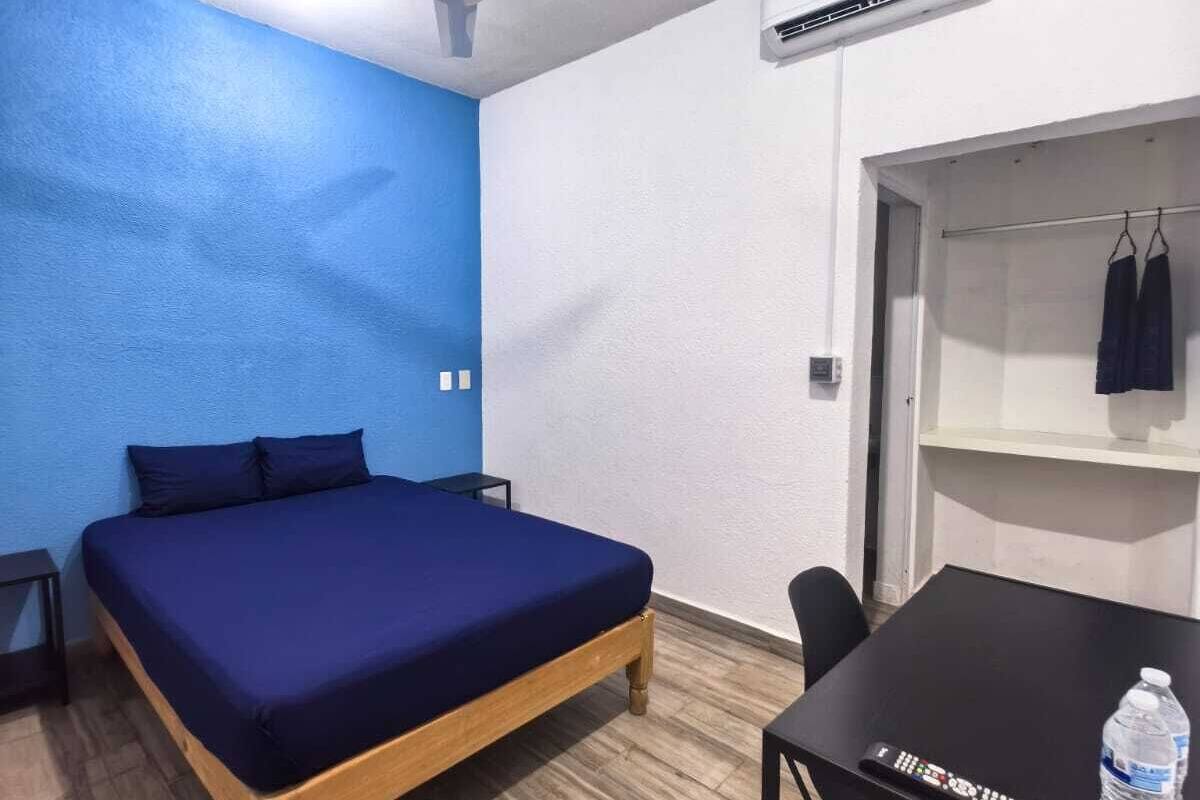 A room with a bed, a desk, a chair, a ceiling fan, and an air conditioning unit.