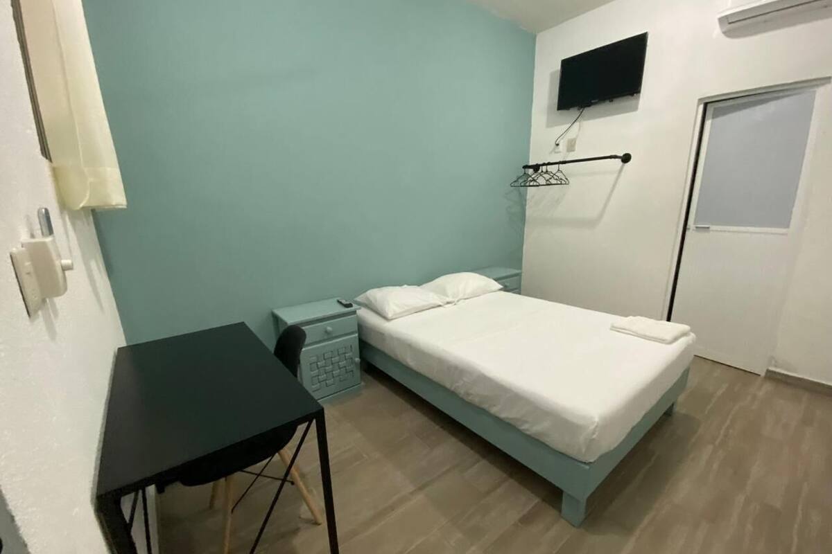 A small, single-bed room with a desk, a TV mounted on the wall, and a door.