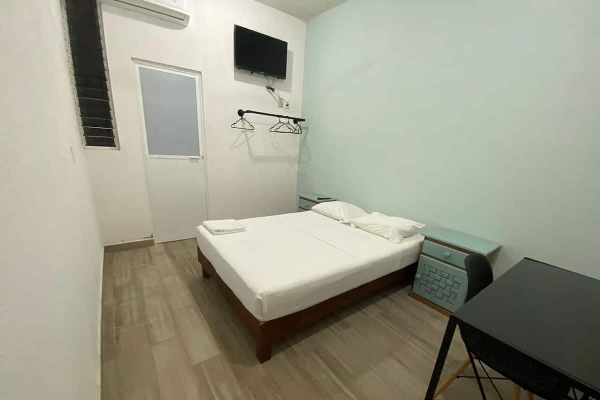 A small, clean room with a bed, a desk, and a TV mounted on the wall.