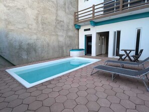 Een zwembad met zeshoekige tegels, ligbedden en een gebouw met een balkon.