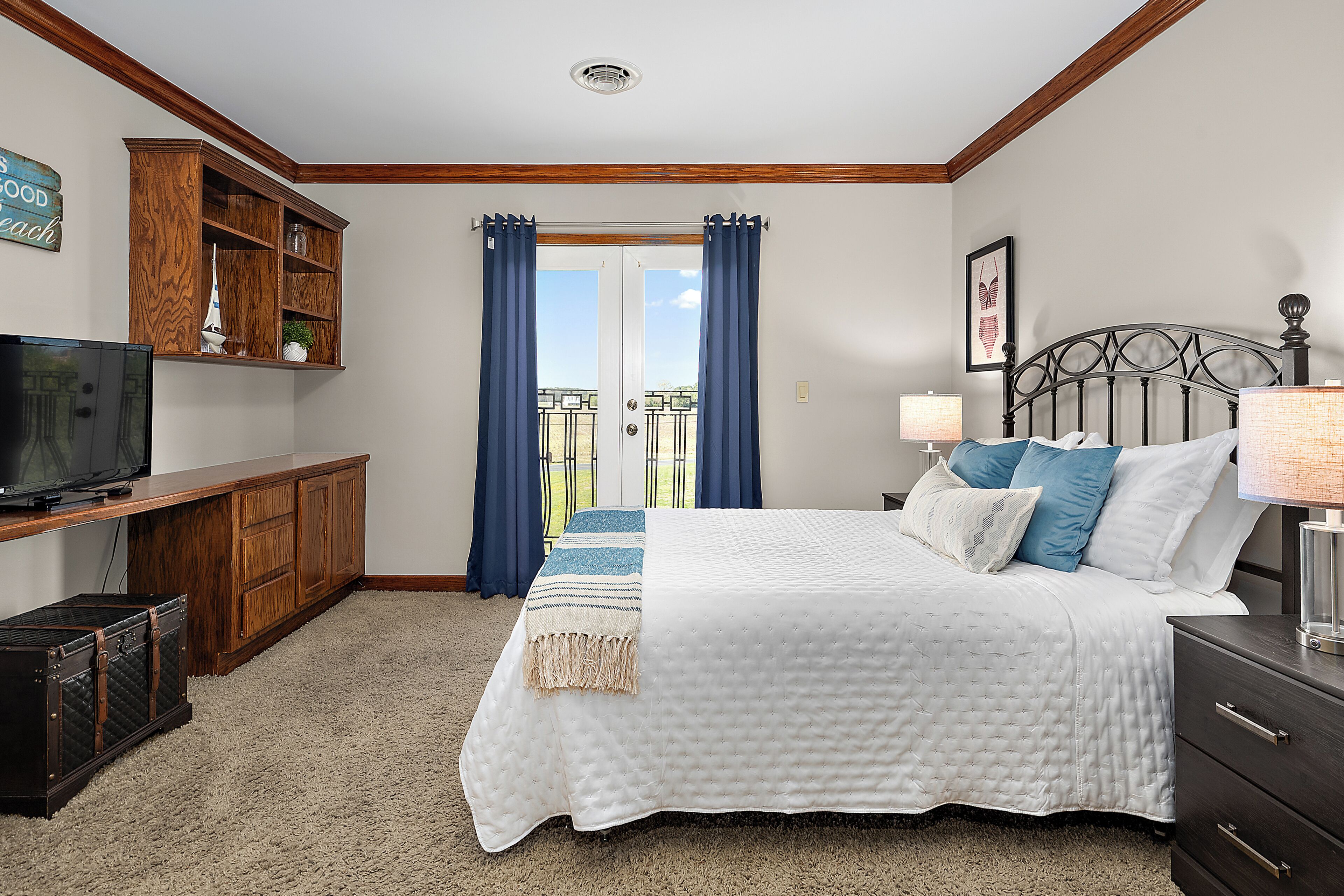 A bedroom with a bed, a television, a dresser, a cabinet, and a balcony view.