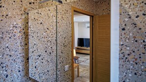 A room with a speckled tile floor, a wooden door, and a television in the background. - Les Mûriers (Calvi)
