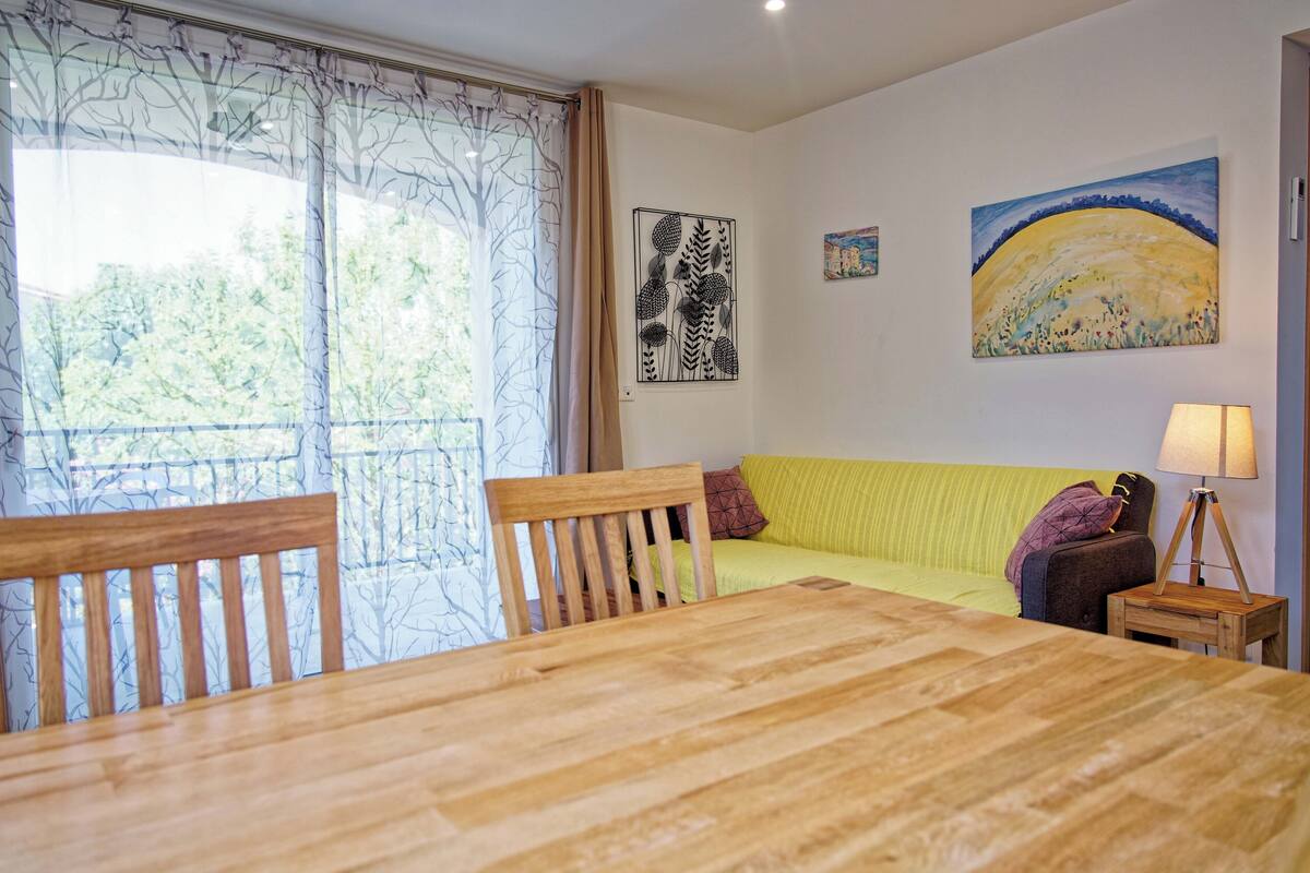 A dining area with a wooden table and chairs, a sofa with cushions, and a painting on the wall.